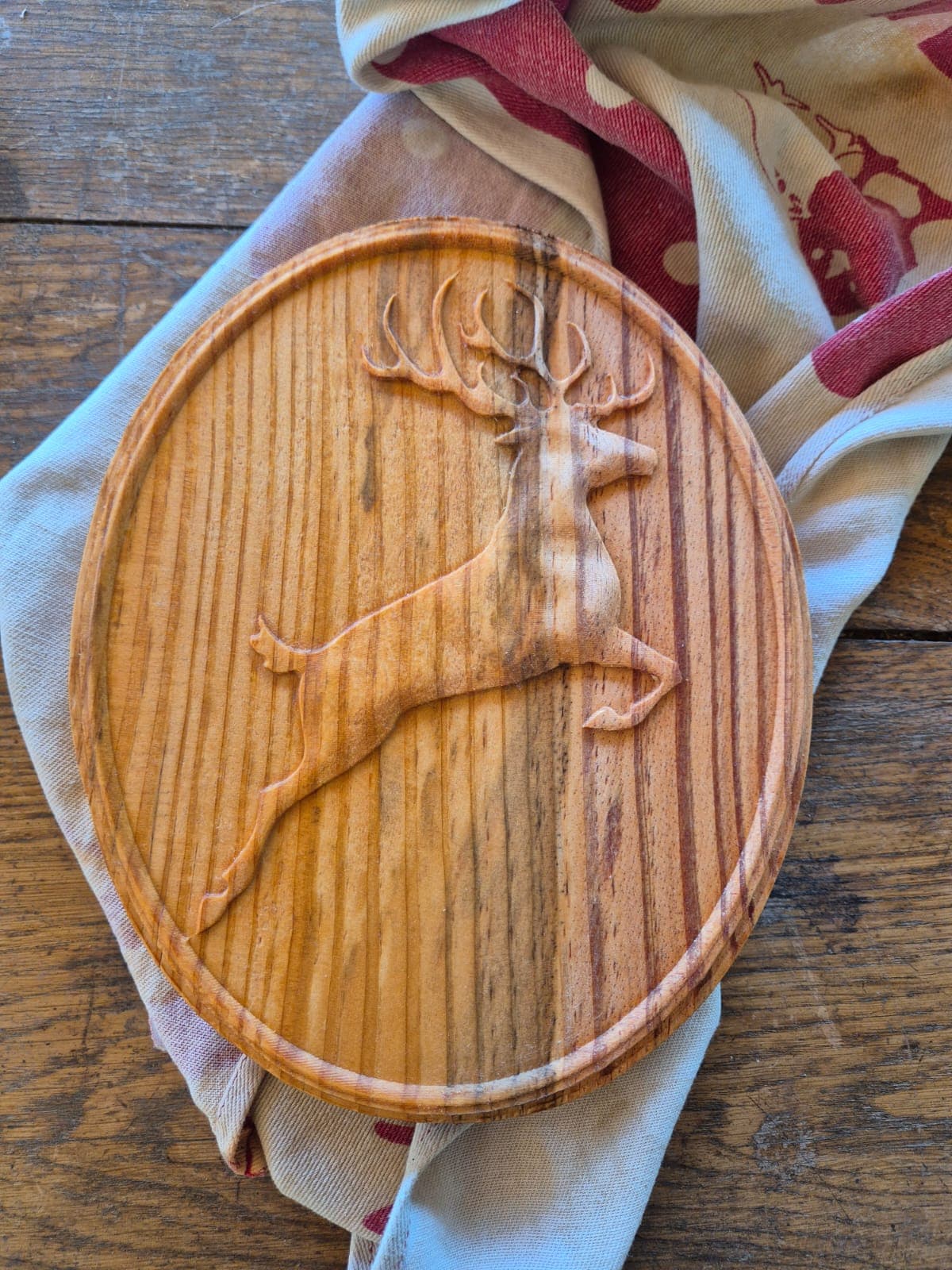 Cerf élancé sculpté en relief sur un médaillon ovale en bois, posé sur une table