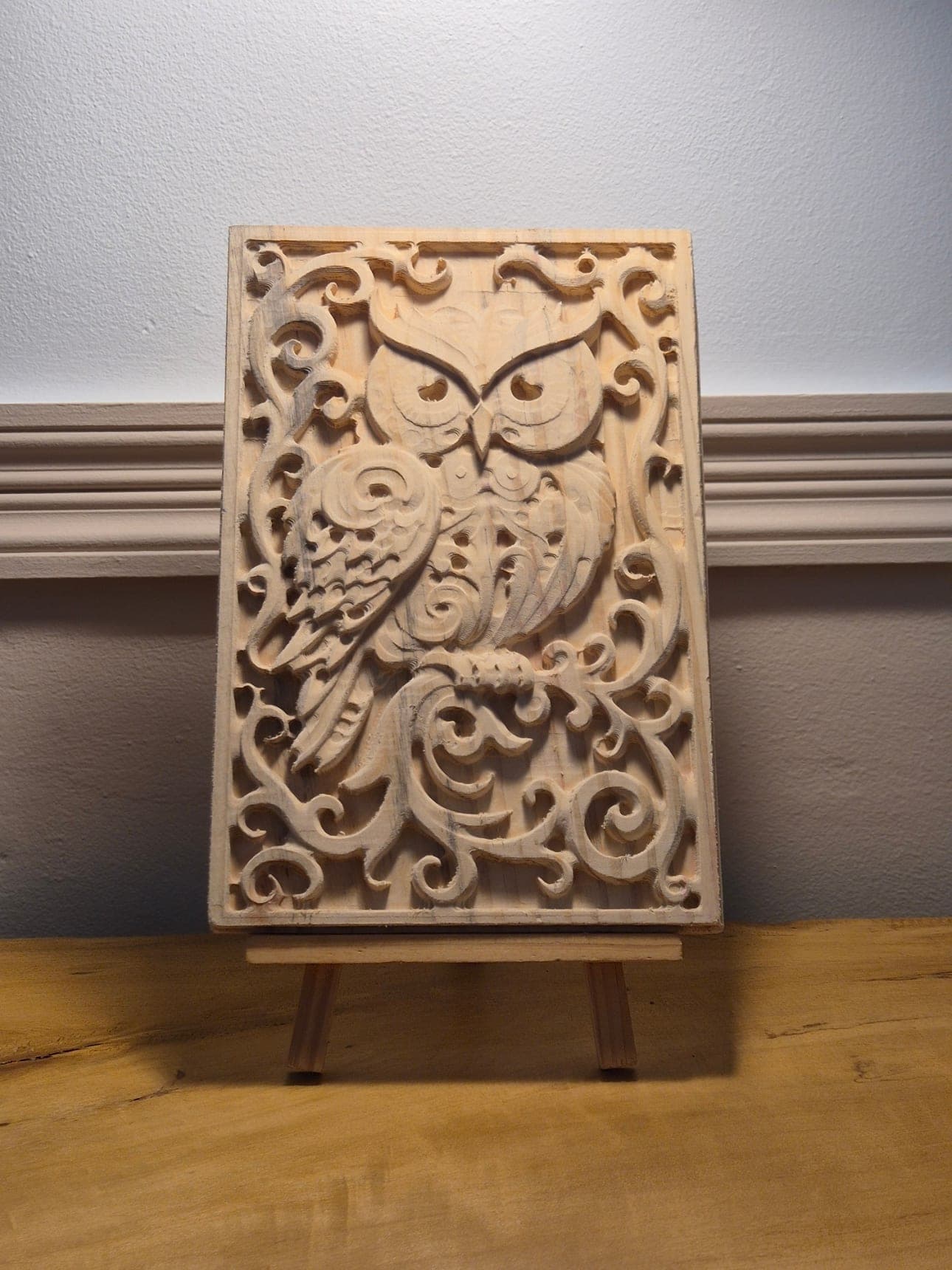Panneau Chouette Flamboyante : chouette sculptée entourée de volutes, posée sur un chevalet