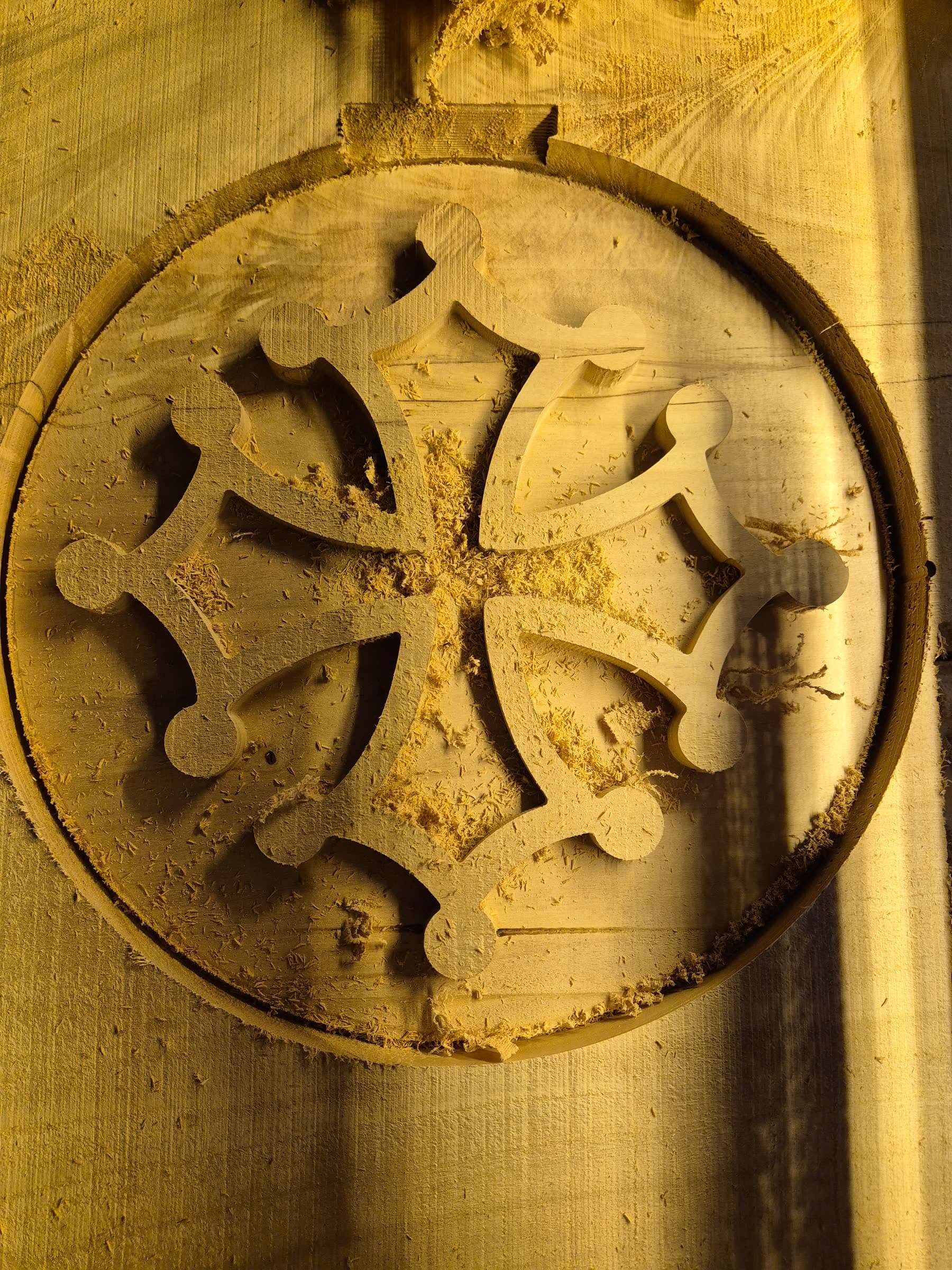 Croix occitane tout juste taillée dans la masse, encore dans son bloc de bois brut couvert de sciure